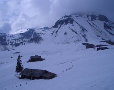 Die Hütten der Genneralm bei bedecktem Wetter, dahinter die steil aufragende Flanke des Gennerhorns.